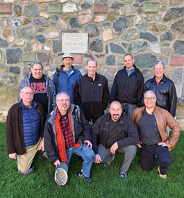 Nine men pose in front of an exterior wall of the Castle.